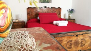 A bedroom with a wooden headboard, red bedding, a bedside table with a lamp, and a vase with flowers. - Comfortable apartment for exclusive use (Valderice)
