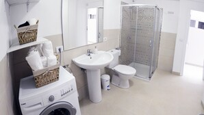 Une salle de bain moderne équipée d’un lave-linge, d’un évier, de toilettes et d’une douche à parois de verre.