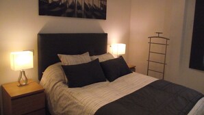 A neatly made bed with a dark headboard, two bedside lamps, and a painting above the bed. - Barrañan beach apartments, Apartment 22 (Arteixo)