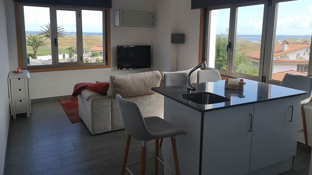 A modern kitchen with a central island, large windows with a view, and a flat-screen TV mounted on the wall. - Barrañan beach apartments, Apartment 22 (Arteixo)