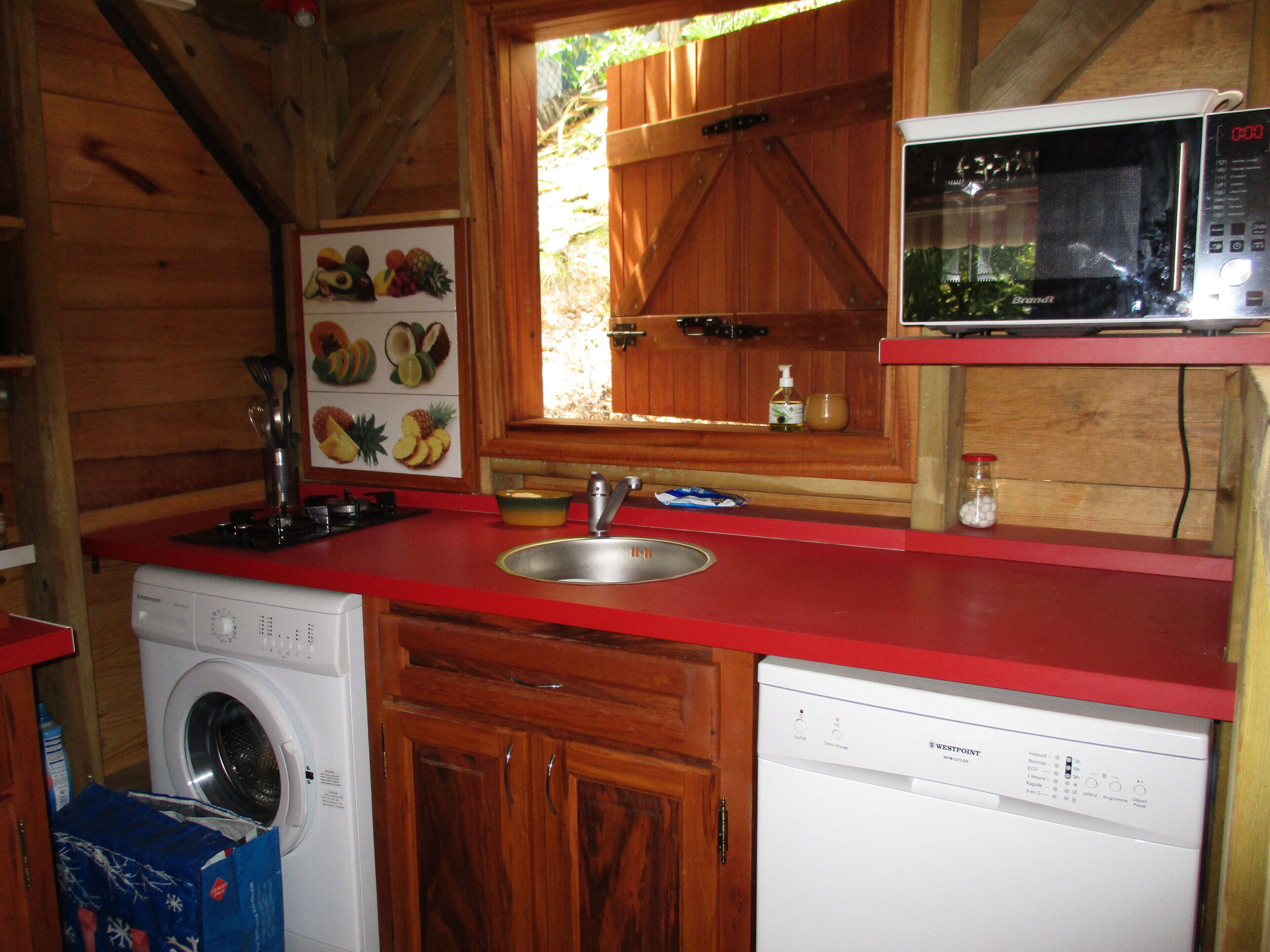 A compact kitchen with wooden cabinets, a red countertop, a washing machine, a dishwasher, and a microwave.