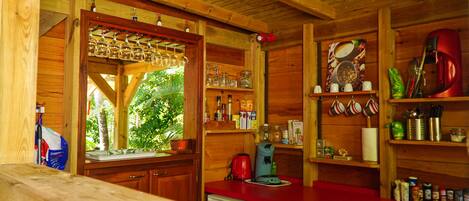 A wooden cabin kitchen with a red countertop, wooden shelves, and a window overlooking greenery.