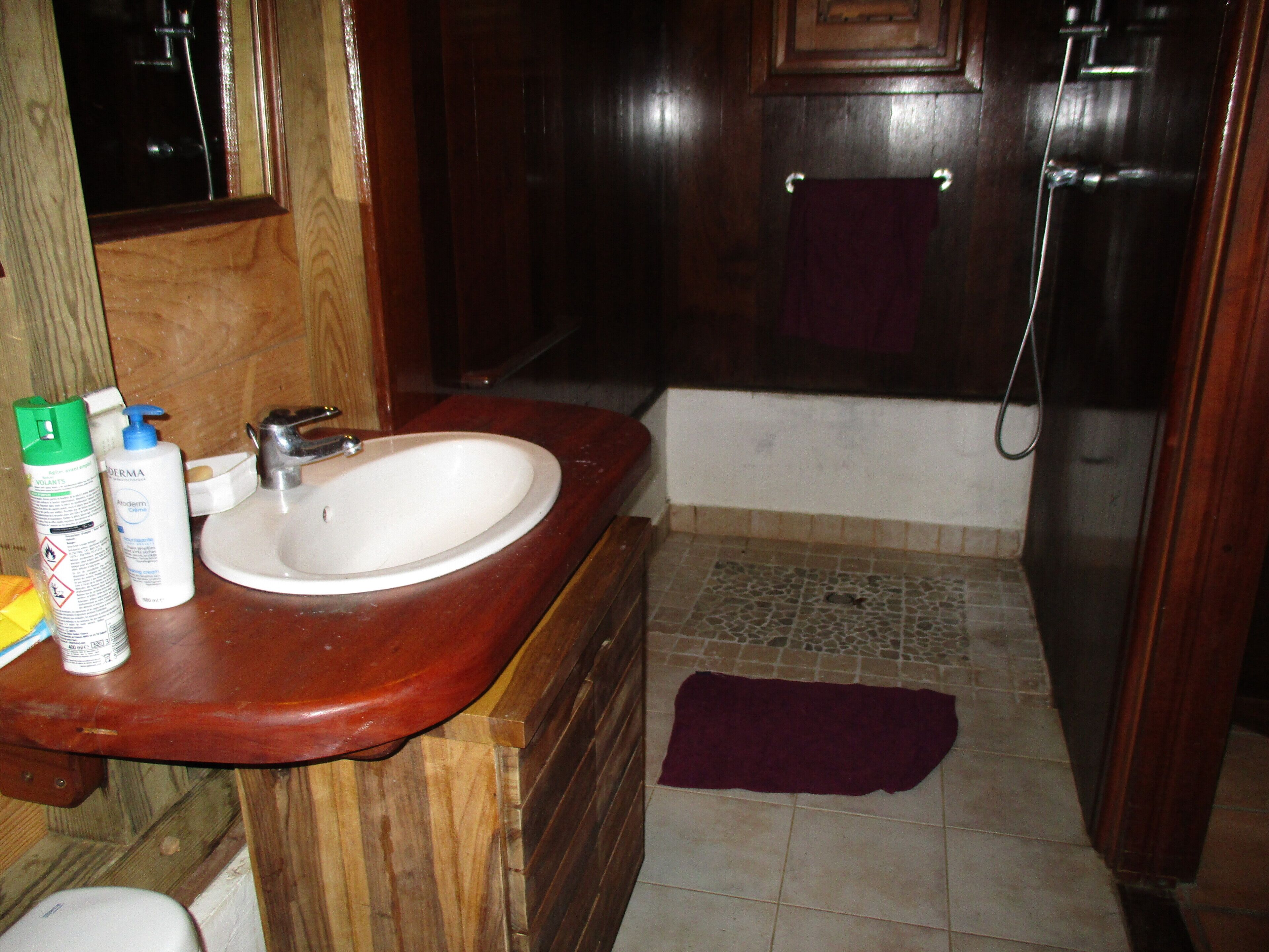 A bathroom with a wooden vanity, a white sink, a mirror, a shower, and a tiled floor.