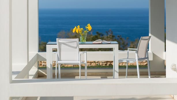 Een wit zitgedeelte buiten met een tafel en stoelen, met uitzicht op de oceaan.