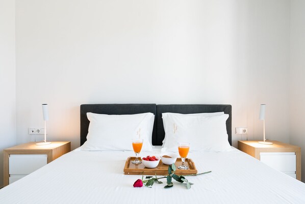 A neatly made bed with white linens, two bedside tables with lamps, a tray with breakfast including fruit and juice, and a single rose on the bed.