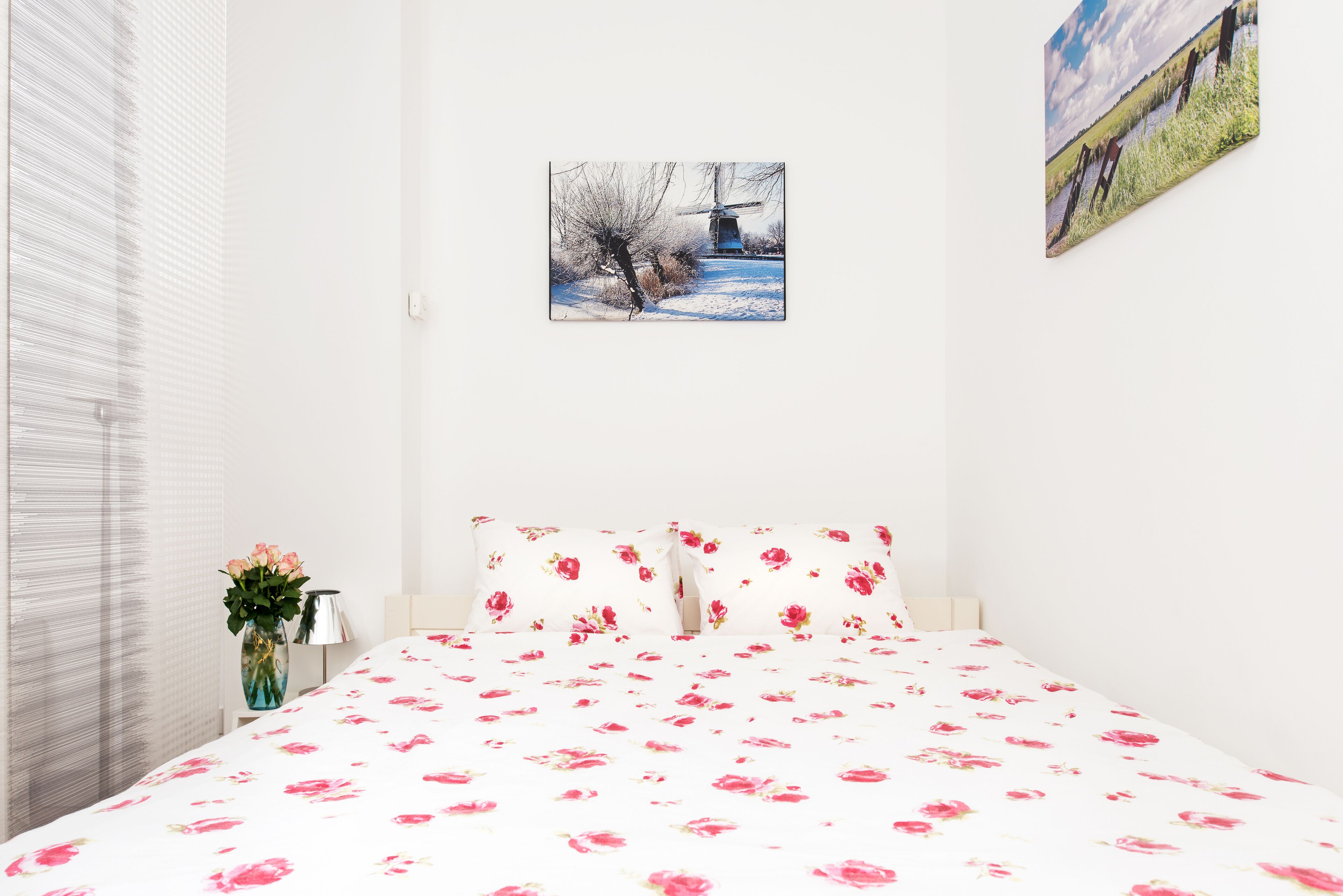 Een slaapkamer met een bed, een vaas met bloemen en een schilderij aan de muur.