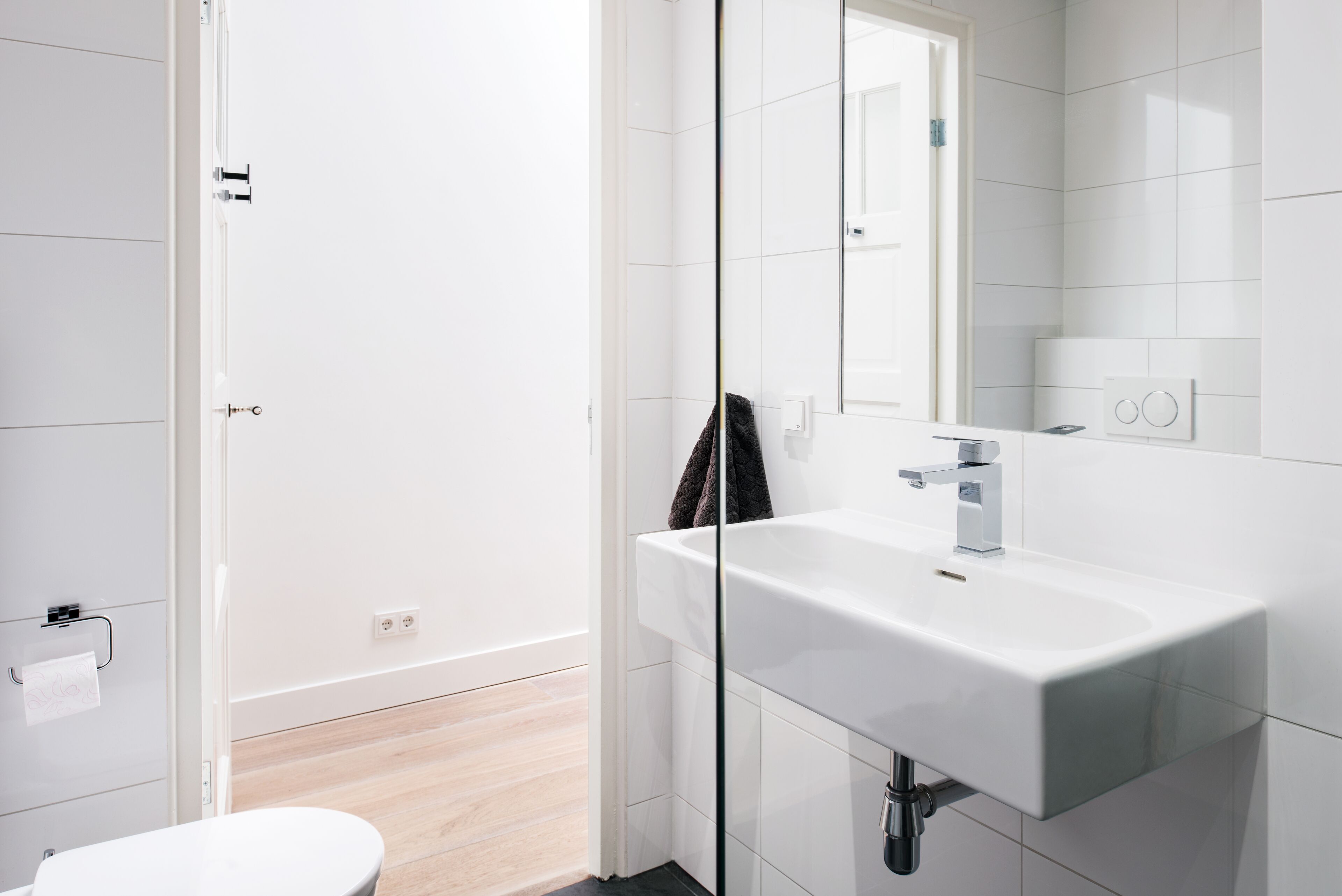 A modern bathroom with a white sink, mirror, and toilet.