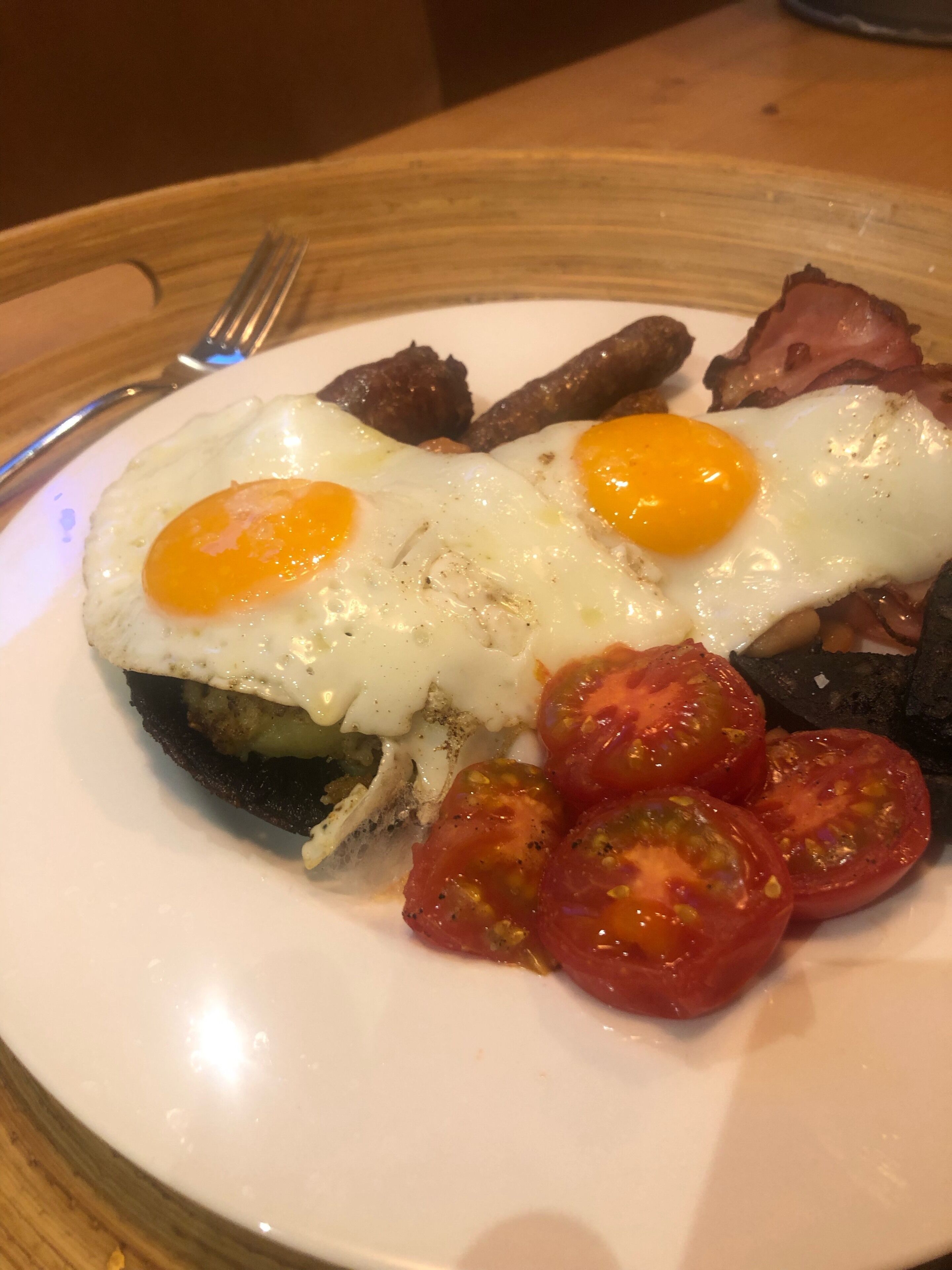 A plate of breakfast food including eggs, bacon, sausages, and tomatoes.