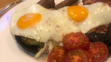 A plate of breakfast food including eggs, bacon, sausages, and tomatoes.
