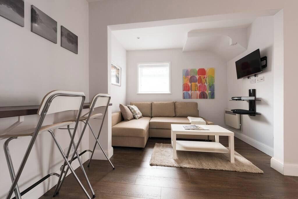 Een moderne woonkamer met een beige bank, een witte salontafel en een aan de muur bevestigde televisie.