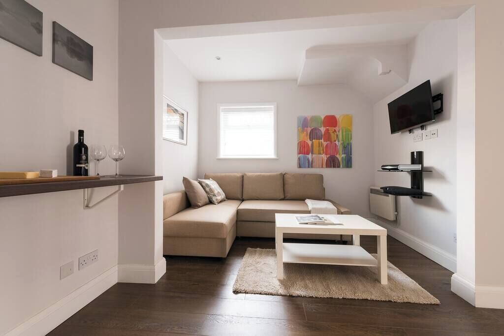A modern living room with a beige sofa, a white coffee table, and a TV mounted on the wall.