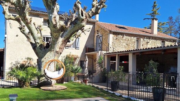 A pool area with a large tree, a swing chair, and a stone building with a tiled roof. - LA MAISON DU MOULIN DE TARTAY EN AVIGNON (Avignon)