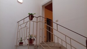 Eine Treppe mit Metallgeländer, Blumentöpfen auf der Zwischenebene und einer Tür zu einem anderen Raum.