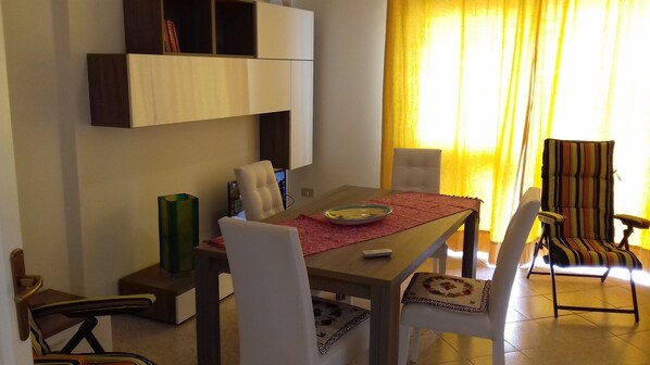 Un coin repas avec une table en bois, des chaises blanches, un set de table rouge et un fauteuil à rayures.