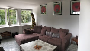 A living room with a sectional sofa, a coffee table, and a window with a view of trees. - Single-storey house 125 m² facing the sea, patio with barbecue and garden. (Crozon)