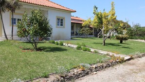 A two-story house with a red-tiled roof, a small garden with various plants, and a stone pathway leading to the entrance. - Farmhouse with large outdoor garden, private, near the beach, very green and quiet (Alfeizerão - São MArtinho do porto)