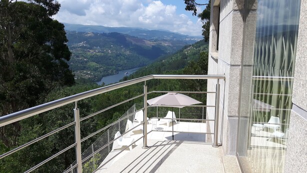 A balcony with a metal railing overlooking a scenic valley with a lake and mountains.