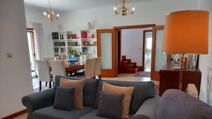 A living room with a grey sofa, a coffee table with books, a bookshelf, and a staircase leading to another room.
