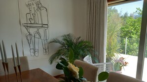 A dining area with a wooden table, white chairs, a vase with white flowers, and a wall art depicting a dining scene.