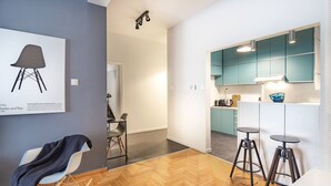 Una cocina moderna con armarios azul verdoso, encimera blanca y dos taburetes de bar.