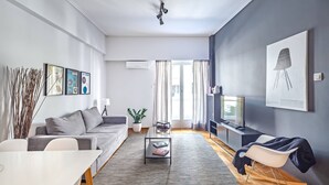 Una sala de estar moderna con un sofá gris, una mesa de centro de vidrio, un televisor sobre un mueble bajo y una mecedora.