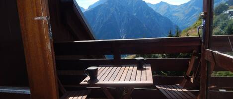 Une terrasse en bois avec une table et des chaises, offrant une vue sur une chaîne de montagnes.