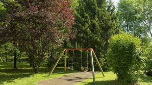 Une balançoire dans un parc, avec une zone pavée et une végétation luxuriante.