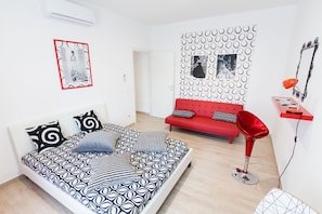 Een moderne slaapkamer met een bed met dessin, een rode bank, een rode fauteuil en een muur met ronde patronen.