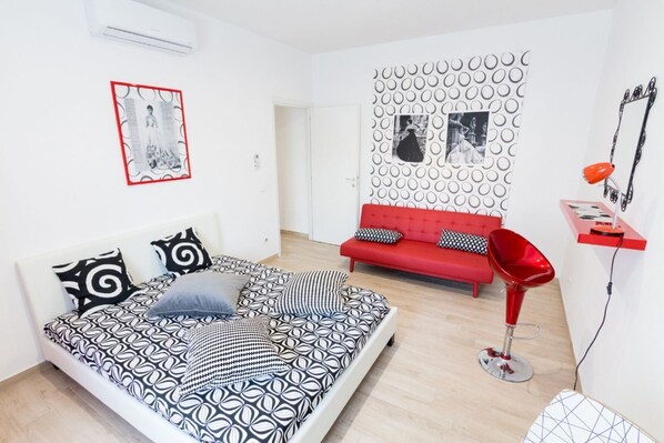 Une chambre à coucher moderne avec un lit à motifs, un canapé rouge, un fauteuil rouge et un mur orné de motifs circulaires.