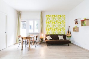 Een woonkamer met een bank, een eettafel met stoelen, een gitaar en een behang met een patroon.