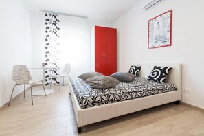 Een slaapkamer met een bed, een rode kledingkast, een bureau met stoel en een raam met gordijn.