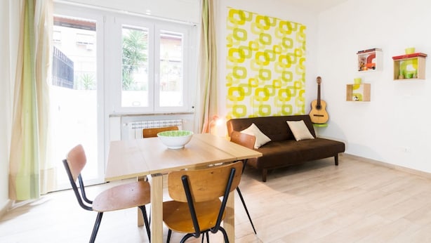 A living room with a sofa, a dining table with chairs, a guitar, and a patterned wall. - Vintage Apartment Trastevere St. (Roma)
