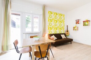 Un salon avec un canapé, une table à manger et des chaises, une guitare et un mur décoré de motifs.