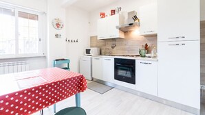 A modern kitchen with white cabinets, a microwave, a dishwasher, and a stove. There is a window with blinds, a table with a polka dot tablecloth, and a small kitchen island. - Vintage Apartment Trastevere St. (Roma)