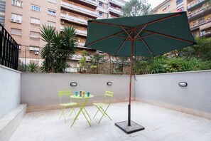A patio with a table and chairs, an umbrella, and a building in the background.