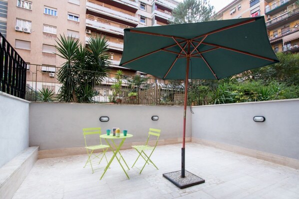 A patio with a table and chairs, an umbrella, and a building in the background.