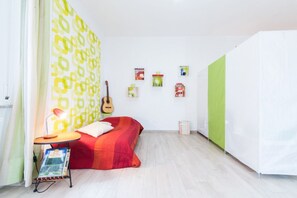 Une pièce avec un lit, une guitare, une petite table avec une lampe et un mur orné de tableaux.