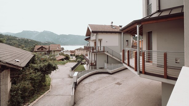 A residential building with a balcony, a view of the mountains, and a body of water in the background.
