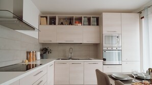 A modern kitchen with a built-in oven, microwave, and a sink. There is a dining area with a table set for two, and a small plant on the counter.