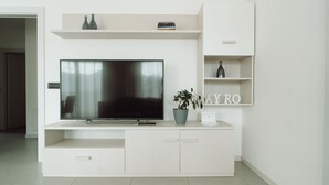 A modern living room with a flat-screen TV, a potted plant, and a shelf with decorative items.