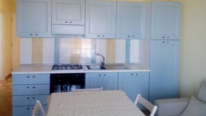 Een kleine keuken met lichtblauwe kastjes, een gasfornuis en een spoelbak.