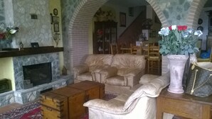 Una sala de estar acogedora con chimenea, un sofá color beige, un cofre de madera y un florero con flores.