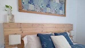 Quarto com cabeceira de madeira, cama com roupa de cama floral azul, almofadas brancas e um espesso acolchoado fixado na parede.