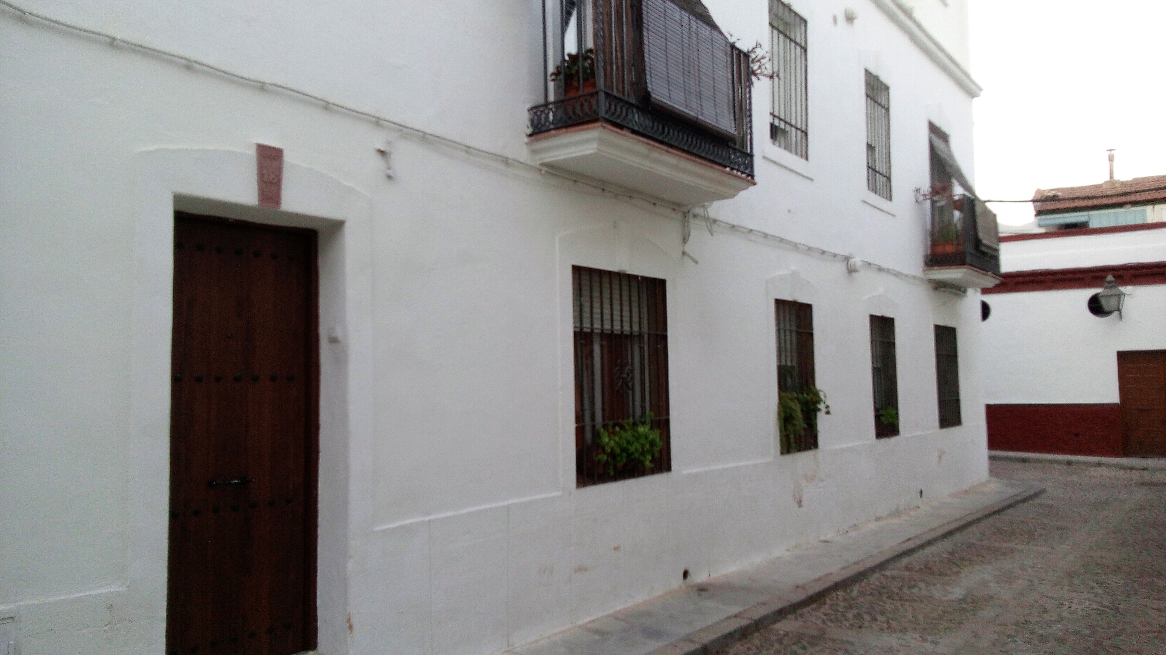 Um edifício branco com porta de madeira, janelas e varanda.