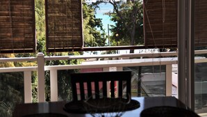 Blick durch ein Fenster mit Jalousien, einem weißen Geländer und einem Tisch mit Unterlage.