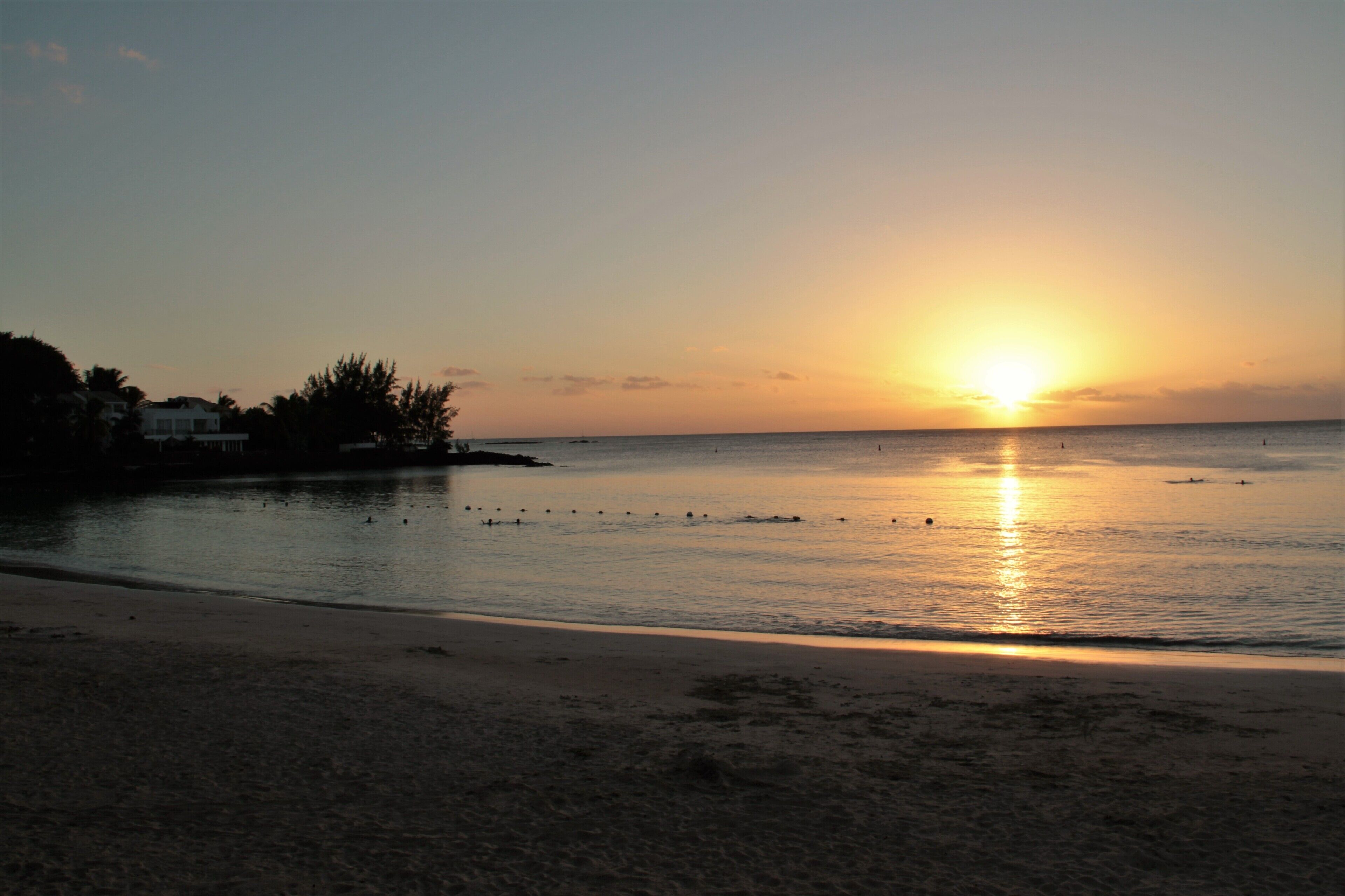 Ein Strand bei Sonnenuntergang, ruhige Gewässer und klarer Himmel.