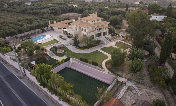 Une grande maison à plusieurs étages, dotée d’une piscine, d’un court de tennis et d’un jardin aménagé.