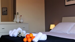 Un lit bien fait, avec du linge de lit blanc, une couvre-lit noire et un bouquet de fleurs et d’oranges sur la table de chevet.
