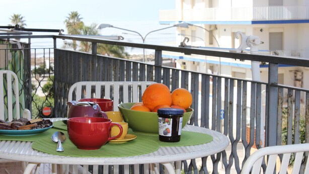 Un balcon avec une table mise pour le petit-déjeuner, comprenant un bol d’oranges, une tasse rouge et un pot de confiture.