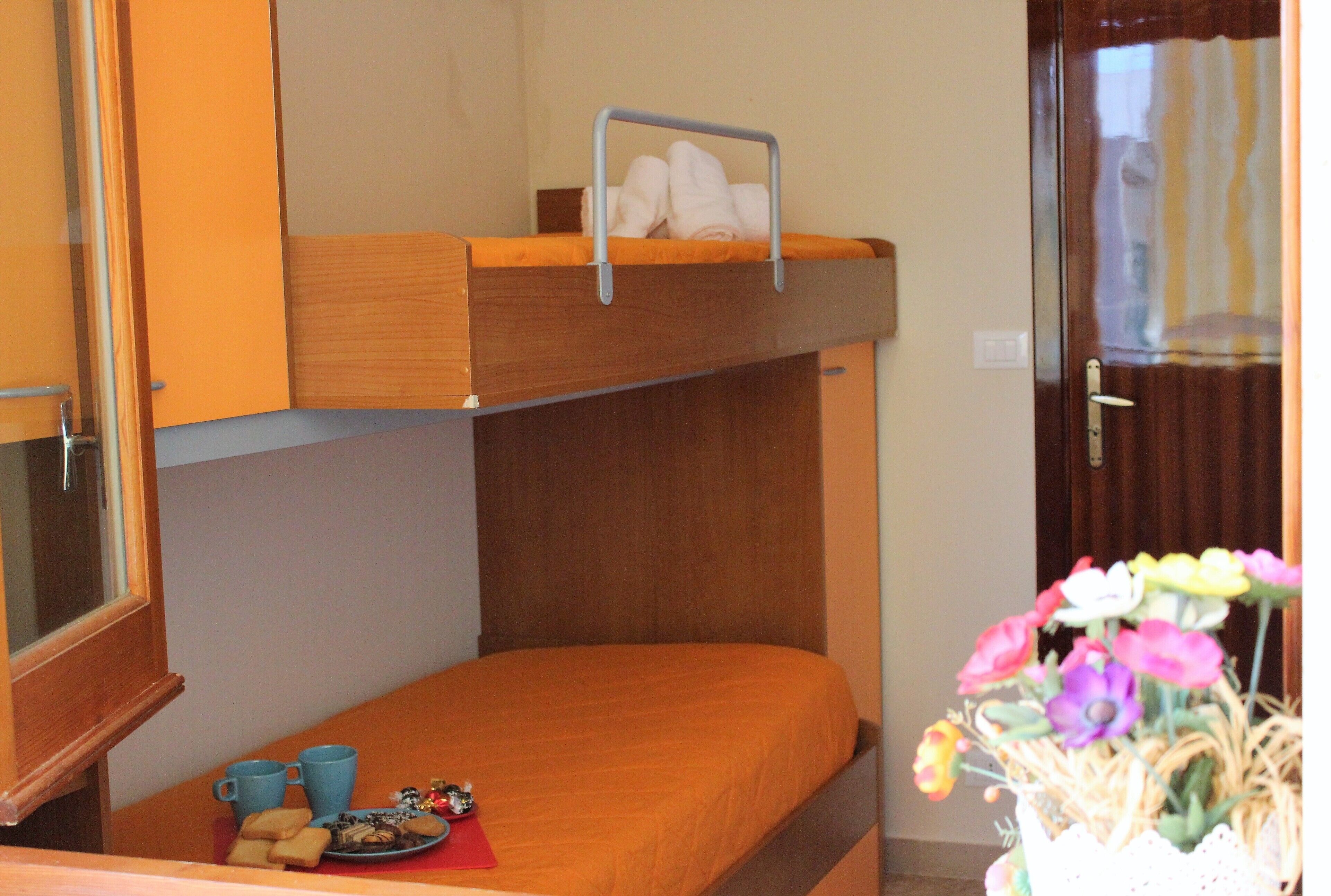A bunk bed with a lower bunk, a small table with a plate of cookies, and a vase with flowers.